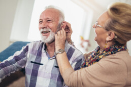 Eldre dame hjelper eldre mann med høreapparatet